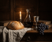 Candlelit still life with a loaf of bread, wine decanter, grapes, and old books.